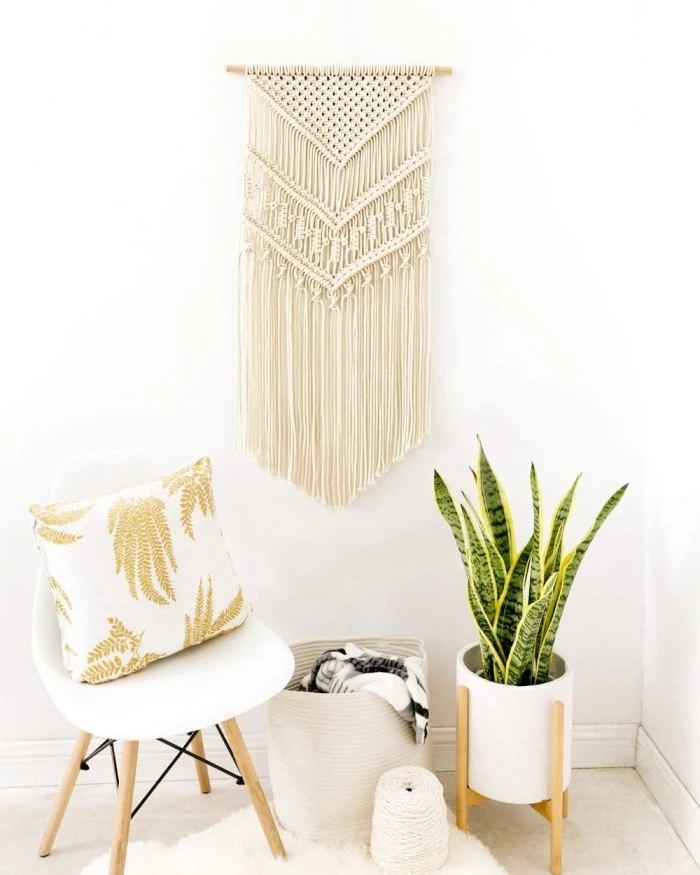 white chair, gold and white throw pillow, macrame wall hanging patterns, white wall, potted plant