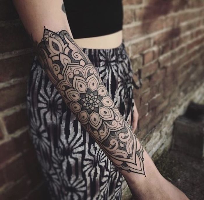 small tattoos with meaning, mandala arm tattoo, black and white pants, brick wall