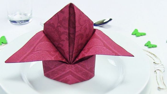 red folded napkin, on a white plate, how to fold dinner napkins, green butterflies around