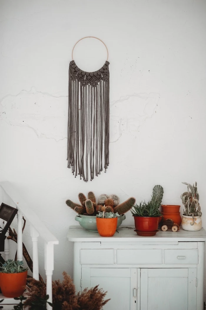 white walls, vintage cabinet, potted cactuses, woven wall tapestry, grey macrame
