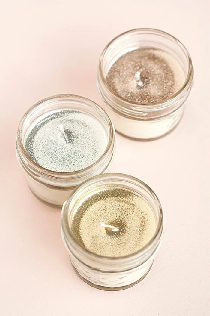 three small glass jars, glitter candle wax inside, how to make scented candles, pink background