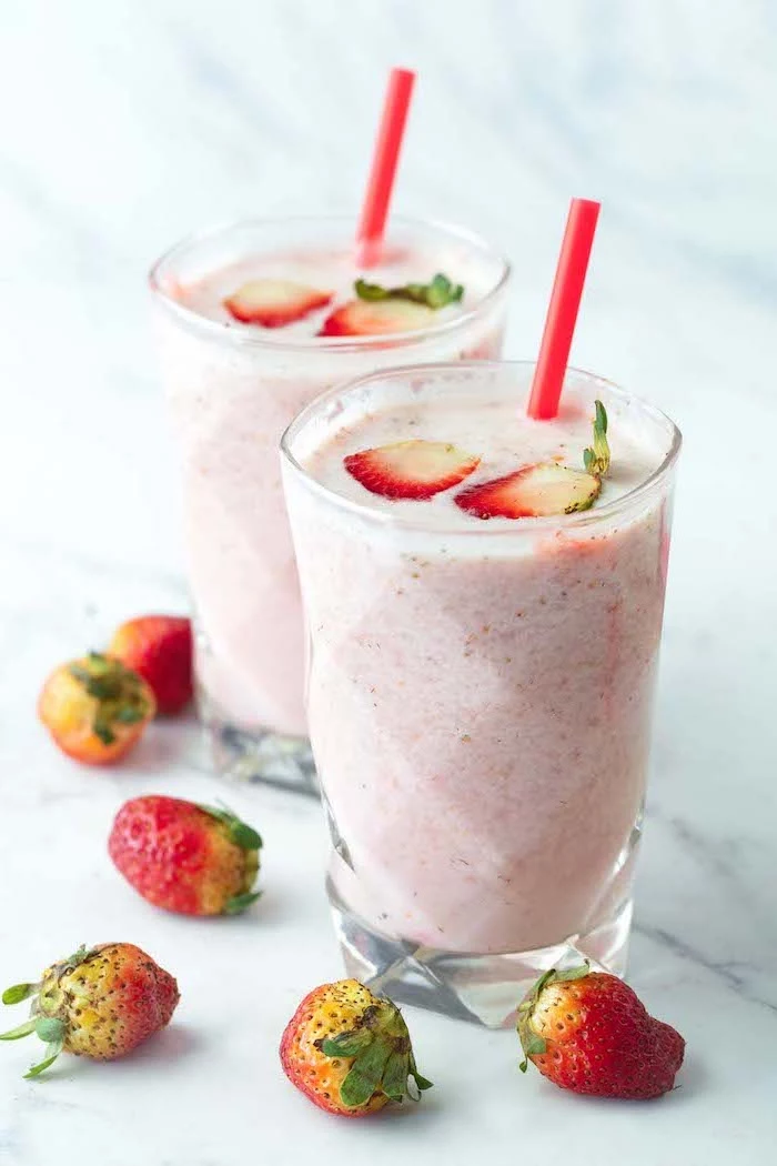 sliced strawberries on top, strawberry banana yogurt smoothie, strawberries around, red straws