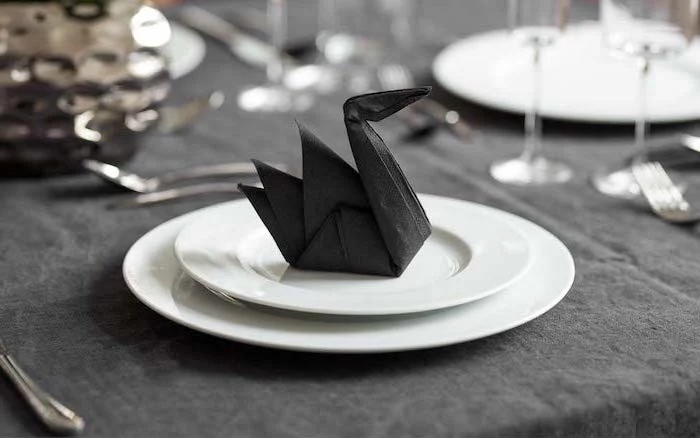 napkin folding ideas, black napkin, in the shape of a swan, on white plates