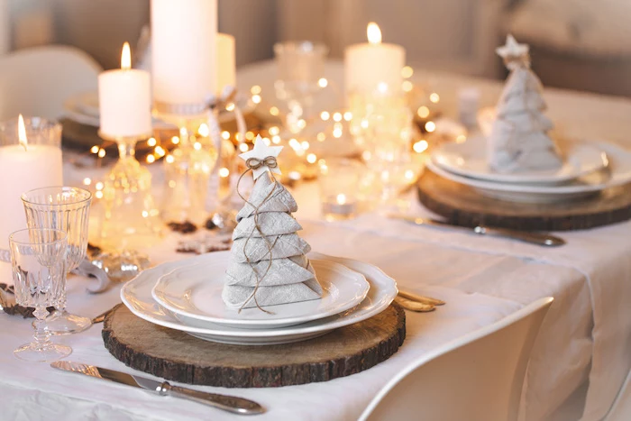 christmas tree shaped white napkins, on white plates, wooden boards, napkin folding ideas, candles and lights