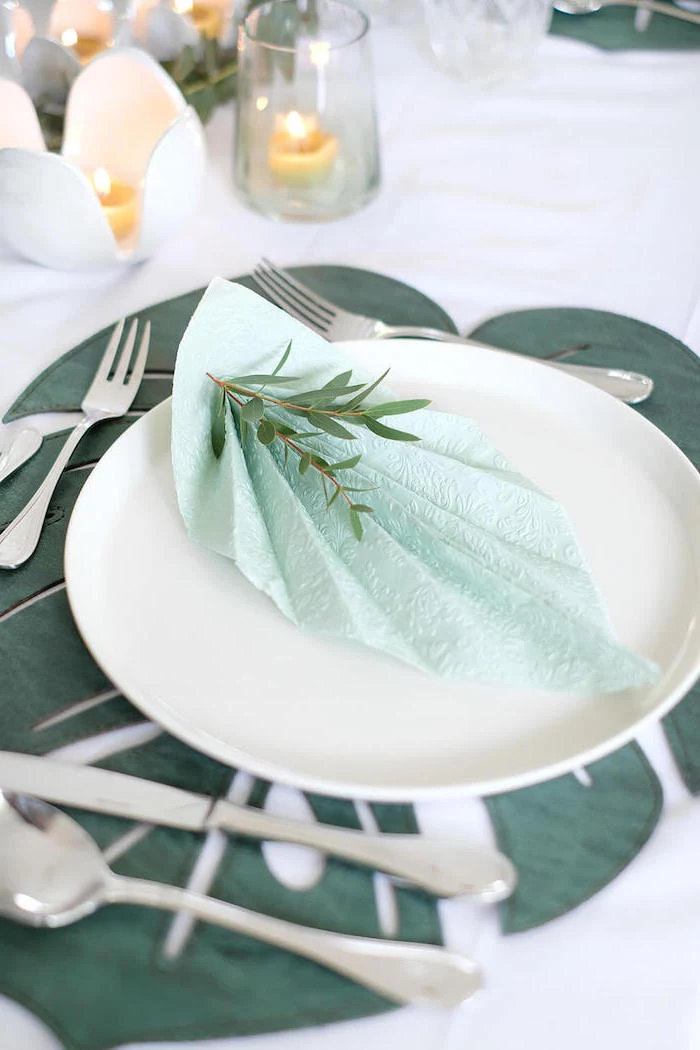 blue napkin, fan shaped, on a white plate, how to fold napkins with rings, silverware arranged