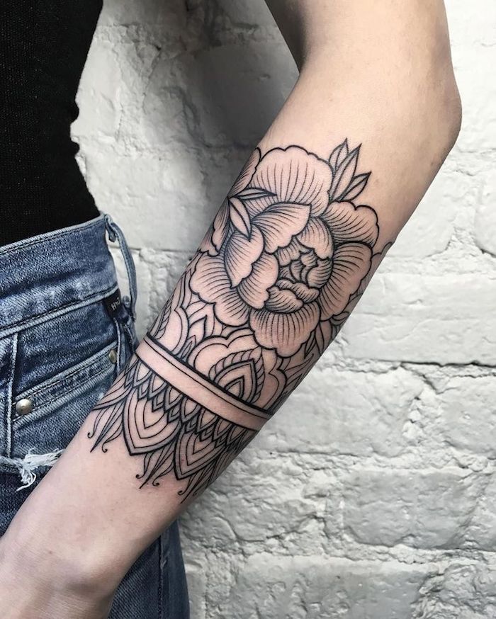 mandala flower tattoo, tattoos for women, white brick wall, black top and jeans