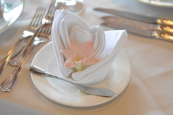 white napkin, flower shaped, pink flower inside, how to fold napkins with rings, on a white plate