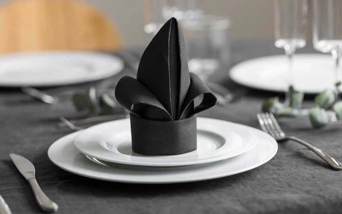black napkin, on white plates, black table cloth, napkin folding with silverware, silverware arranged around it