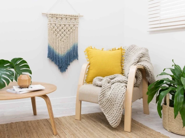 wooden armchair, knitted grey blanket, woven wall hanging, wooden table, potted plants, white walls