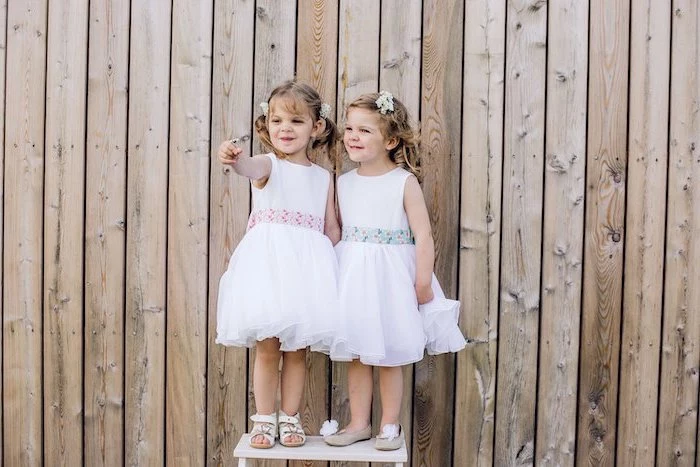 two girls, standing on a white table, wooden background, flower girl shoes, floral ribbon, blonde hair