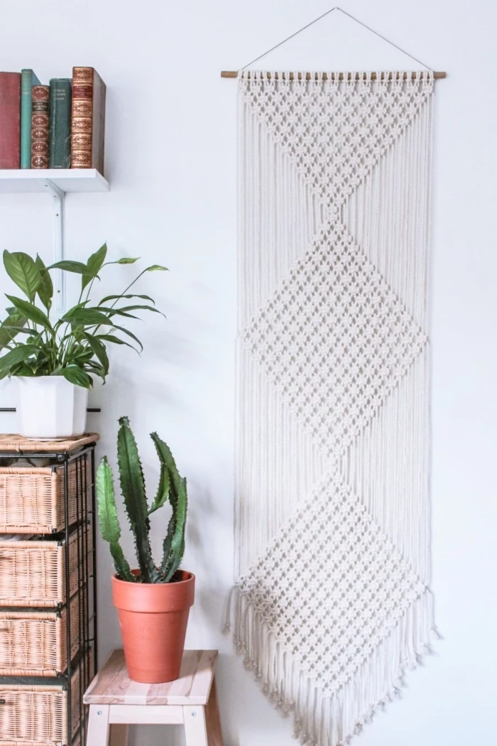 wooden bookshelves and drawers, potted cactus, white wall, woven tapestry wall hanging, small wooden chair