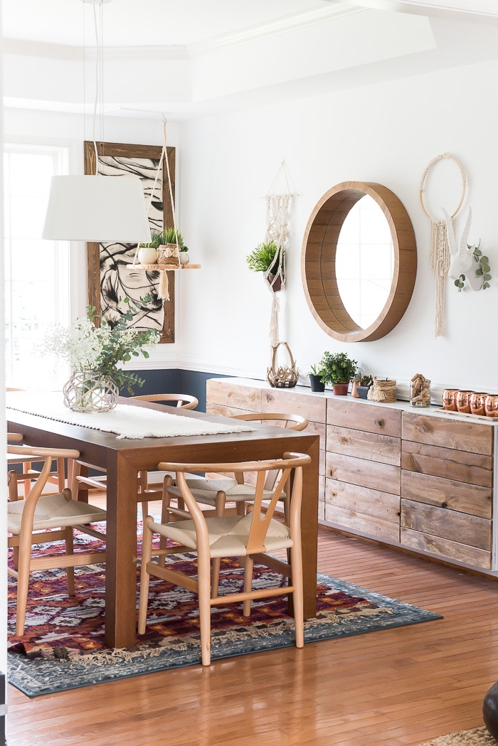 round wooden mirror frame, wooden floor, macrame backdrop, wooden chairs and table, printed rug