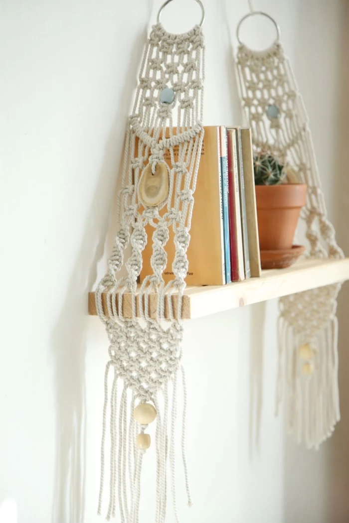 wooden hanging shelf, ceramic pot, stack of books, macrame wall hanging knots, white wall