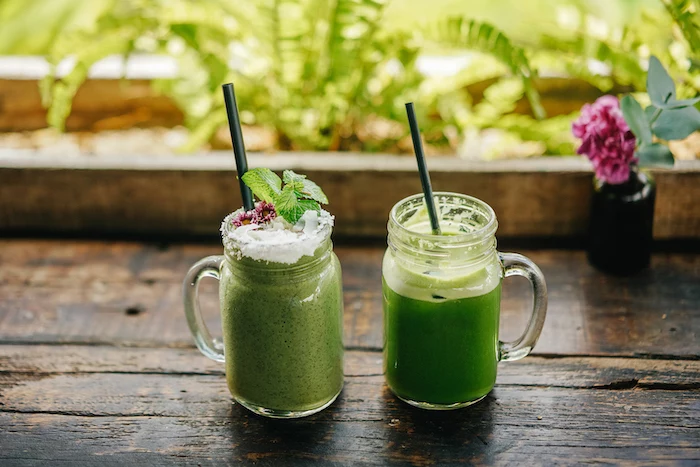 black straws, how to make a green smoothie, on a wooden table, flowers in the background
