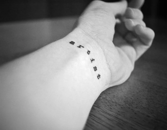 artist wrist tattoo, black and white photo, tattoo placement, wooden table