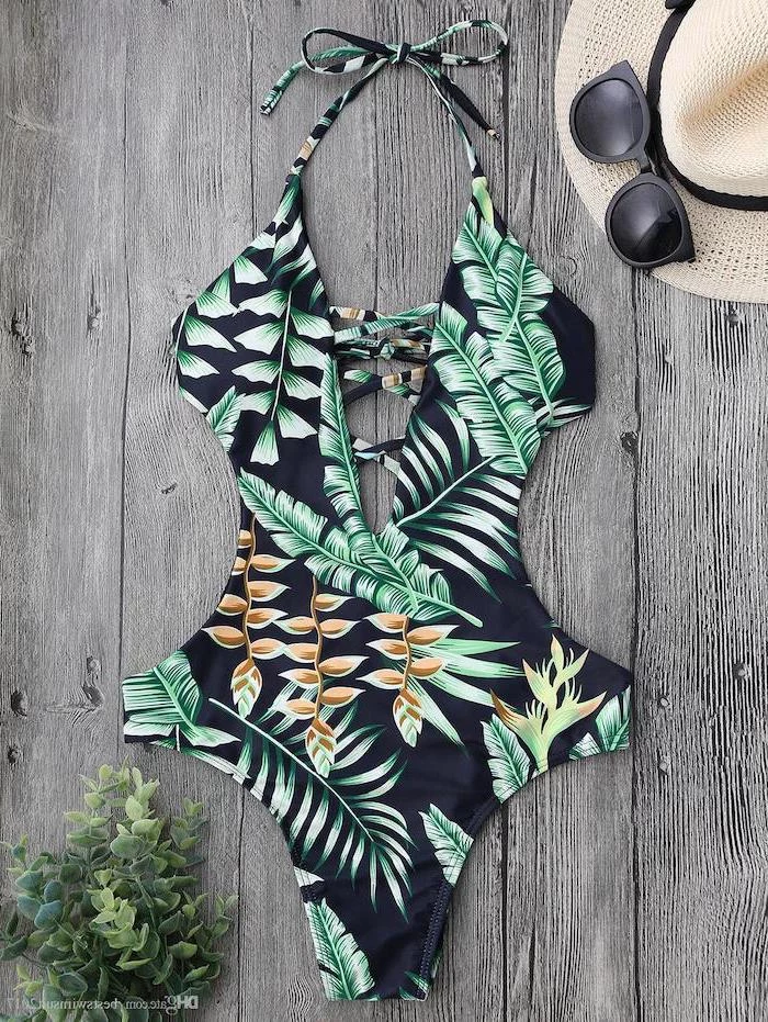 girls one piece swimsuit, in black with green palm leaves print, wooden background, straw hat and sunglasses