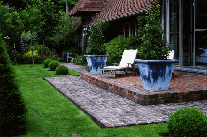 front porch decorating ideas, large blue pots, trees and bushes, brick tiled floor, wooden armchairs