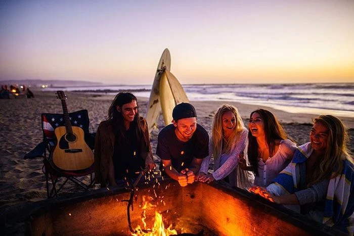 five people, gathered around a fire, on a beach, themes for parties, guitar on a chair, two surf boards