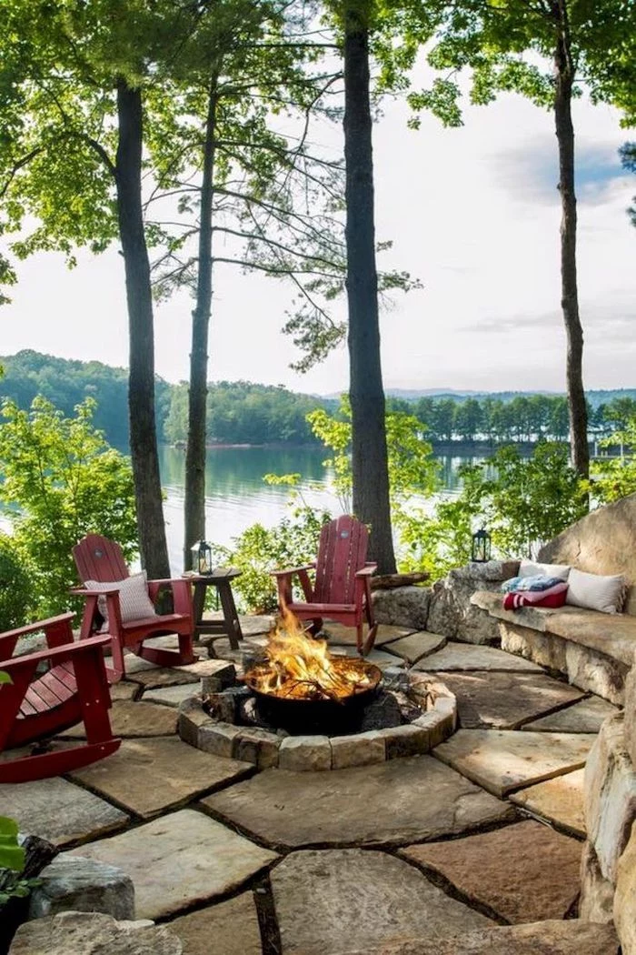 porch decorating ideas, wooden chairs, round fire pit, stone tiles floor, tall trees, over a lake