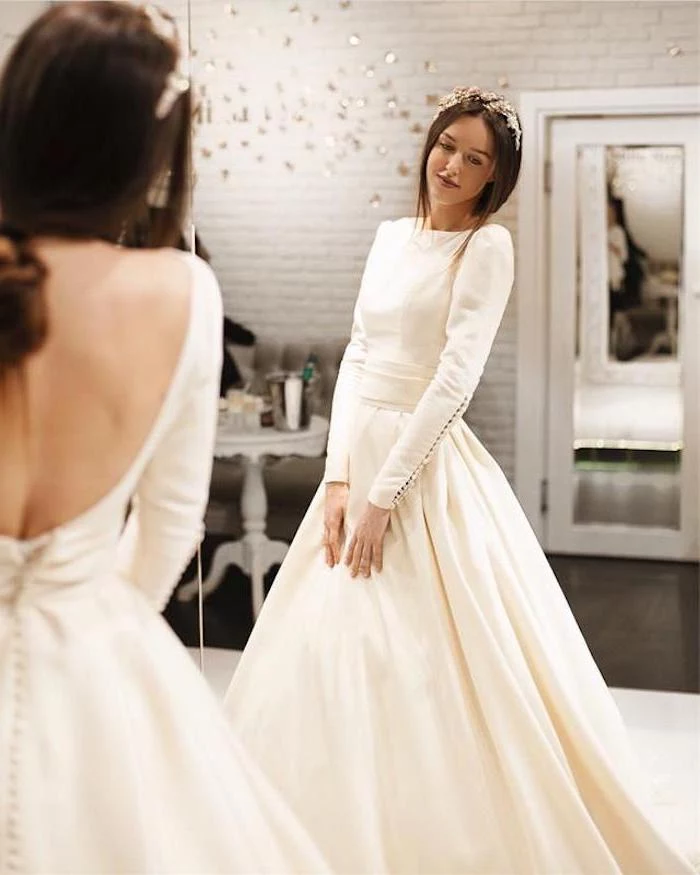 mirror image, bare back, long sleeve ball gown wedding dress, brown hair, in a low ponytail, hair accessory