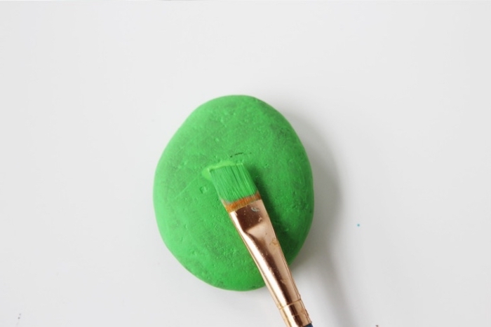 small rock, painted green, with a paintbrush, diys for kids, white background