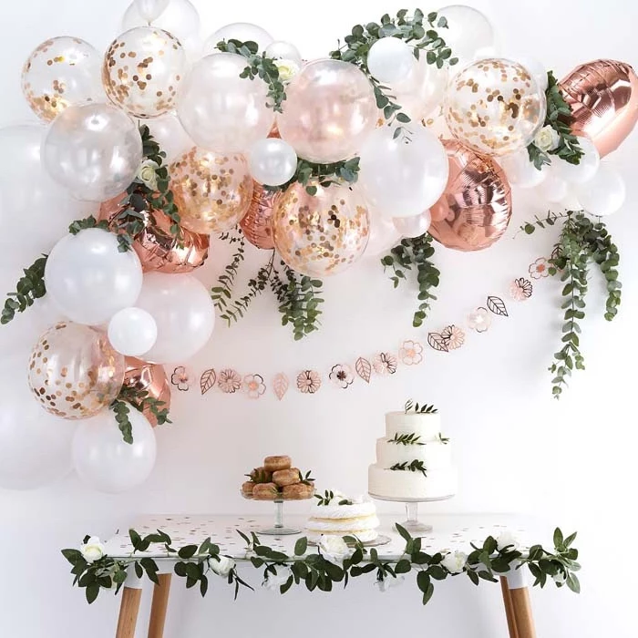 rose gold and white balloons, with confetti inside, theme party ideas, three tier cake, greenery garlands