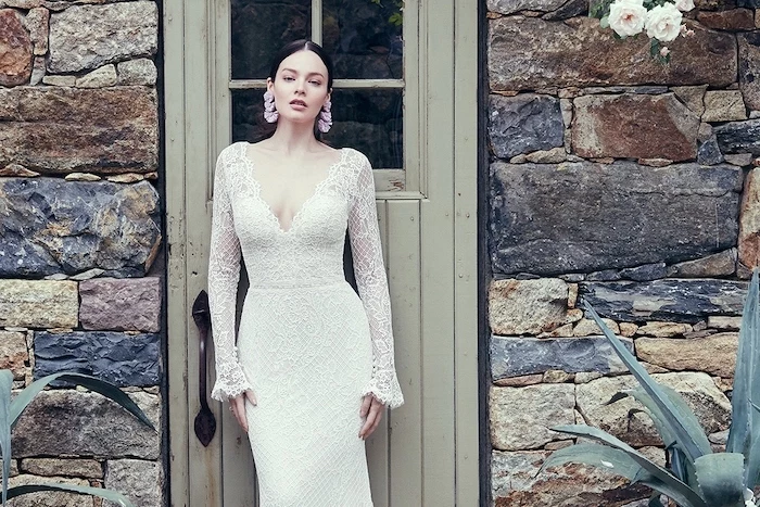 gowns with sleeves, lace dress, v neckline, black hair, in a low updo, wooden door, stone wall