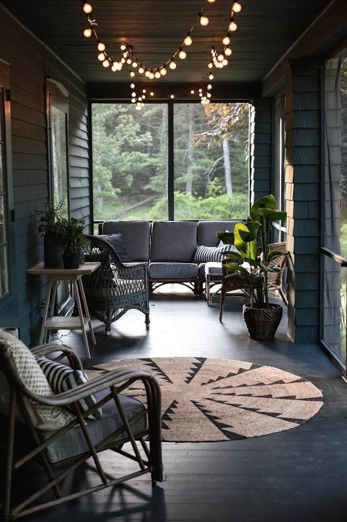 strings of lights, grey sofa, black wooden floor, wooden chairs, potted plants, screened in porch ideas