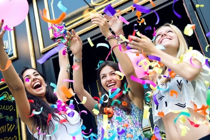 three girls smiling, with their hands up, colourful confetti around them, birthday party ideas for teens