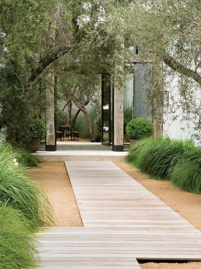 wooden pathway, gravel around it, green bushes, tall trees, front porch railing ideas, garden furniture