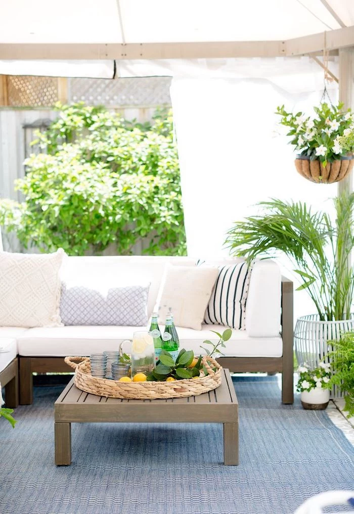 front porch railing ideas, wooden furniture, white cushions, blue rug, hanging potted plants