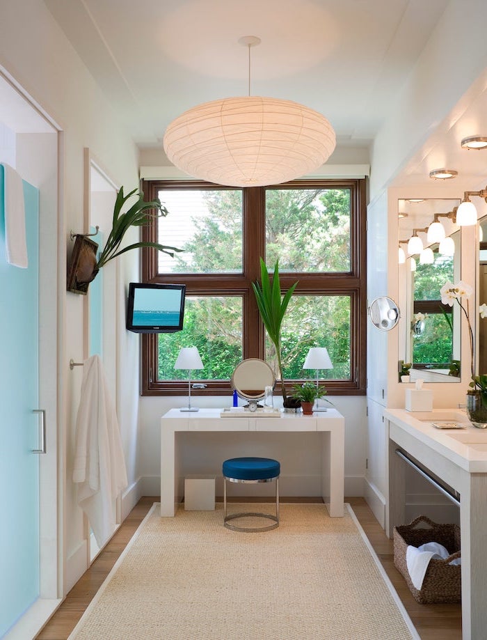 white table, small round mirror, metal stool, blue velvet cushion, makeup vanity with lights, white rug