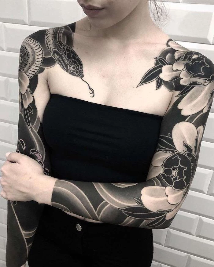 snake and flowers, arm tattoos for women, on both arms, white tiled wall, black top