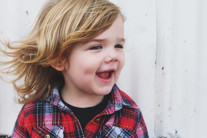 little boy smiling, with blonde hair, medium length, red plaid shirt, little boy haircuts, white background