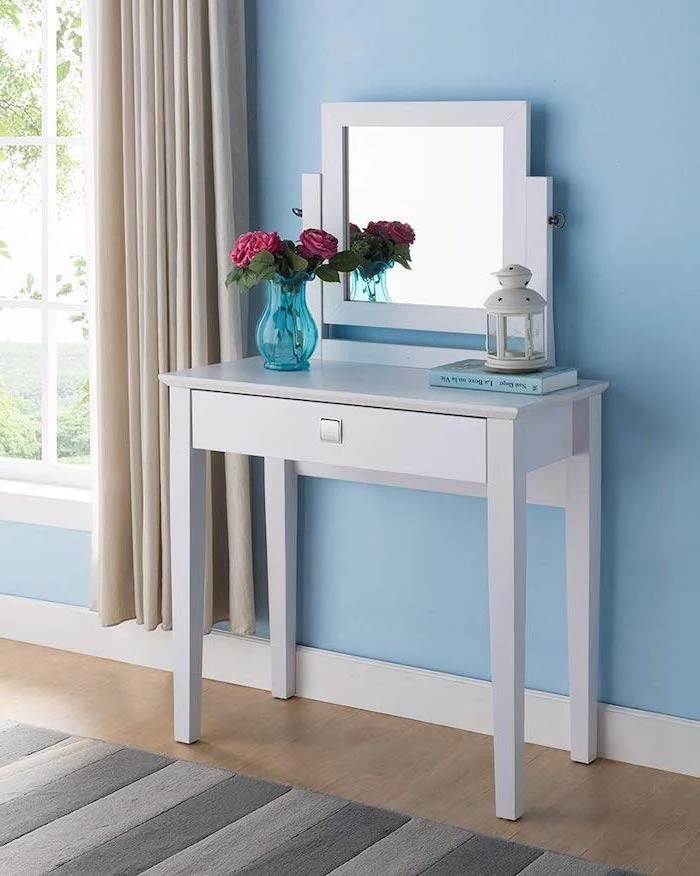 white table, square mirror, black makeup vanity, wooden floor, blue wall, beige curtains