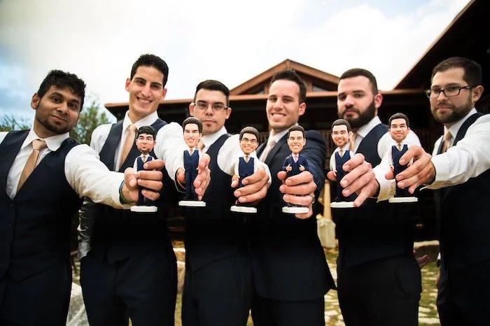six men, holding bobbleheads of themselves, wearing black suits, gold ties, groomsmen gift ideas