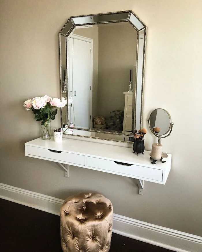 dressing table mirror, floating white shelf, brown velvet ottoman, white wall, roses bouquet