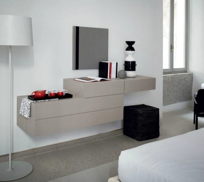 white wall, floating shelves, dressing table mirror, black ottoman, tea set, square mirror