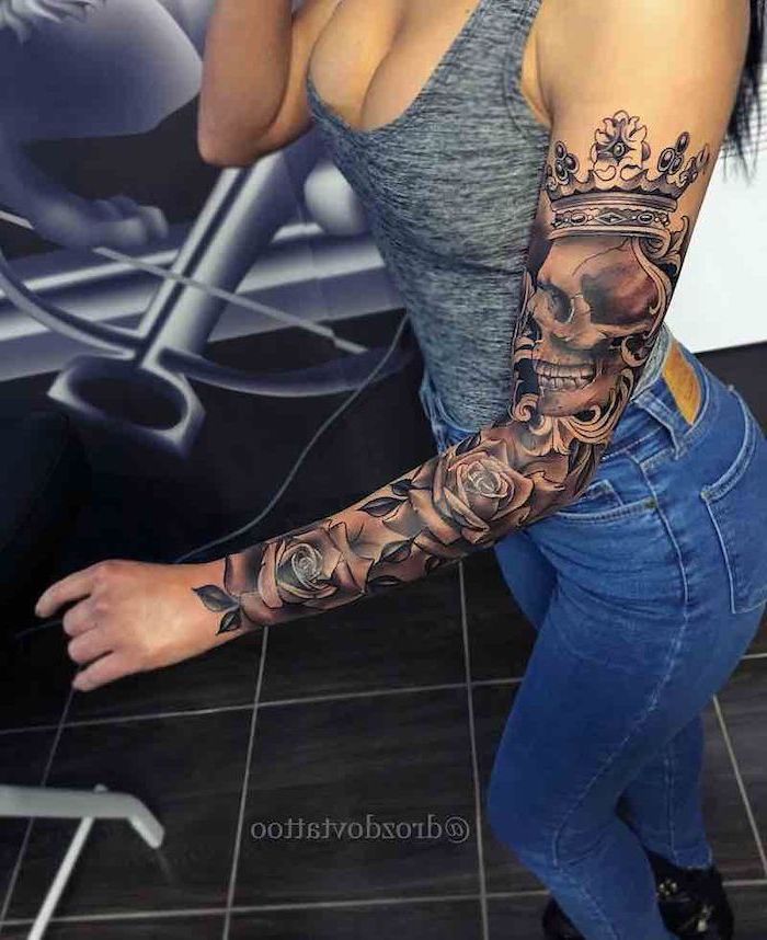 grey top, blue jeans, skull and roses, black tiled floor, lion tattoo sleeve