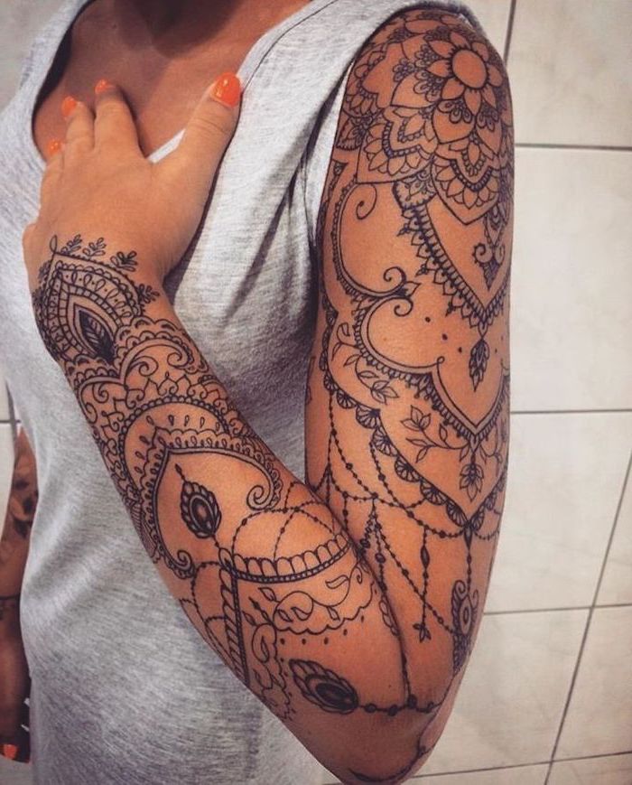 skull sleeve tattoo, floral mandala tattoo, grey top, white tiled wall, orange nail polish