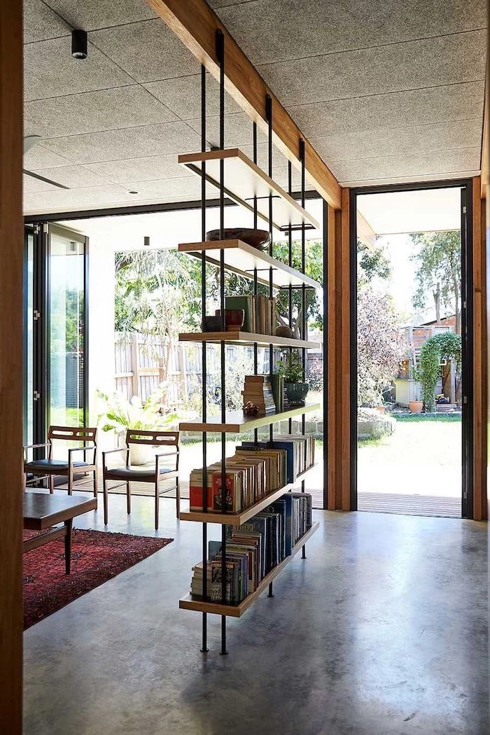 room divider shelves, wooden bookcase, cement floor, tall windows, red carpet, wooden chairs