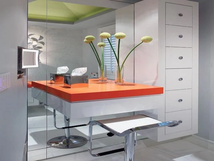 orange floating shelf, metal stool, small makeup vanity, white drawers, large mirror