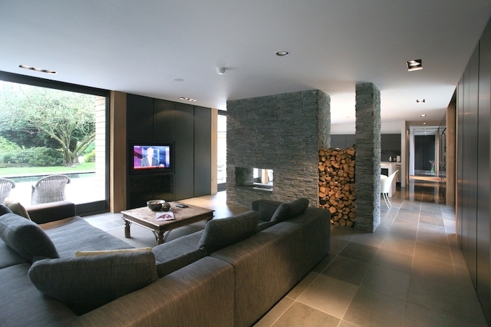stone wall and wood, grey corner sofa, room separator, tiled floor, wooden table, black walls