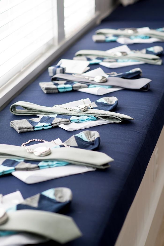groomsmen gift ideas, pair of socks, tie and handkerchief, pocket watch, arranged on a blue ottoman