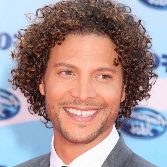 brown curly hair, hairstyles for men with thick hair, man smiling, grey blazer