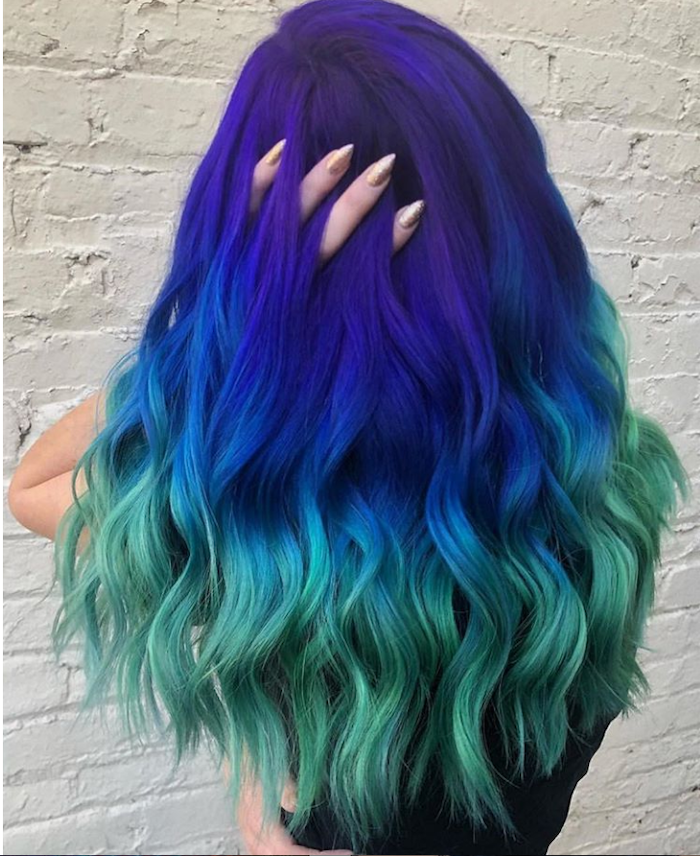 white brick wall, what is ombre hair, purple to blue and green, black top, long wavy hair
