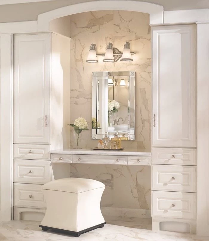 tiled marble wall and floor, white leather ottoman, makeup vanity table with lighted mirror, white drawers