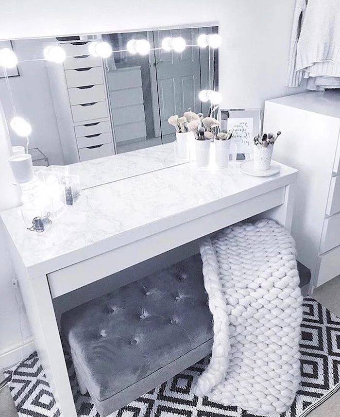 grey velvet ottoman, white knitted blanket, modern makeup vanity, marble countertop, mirror with lights
