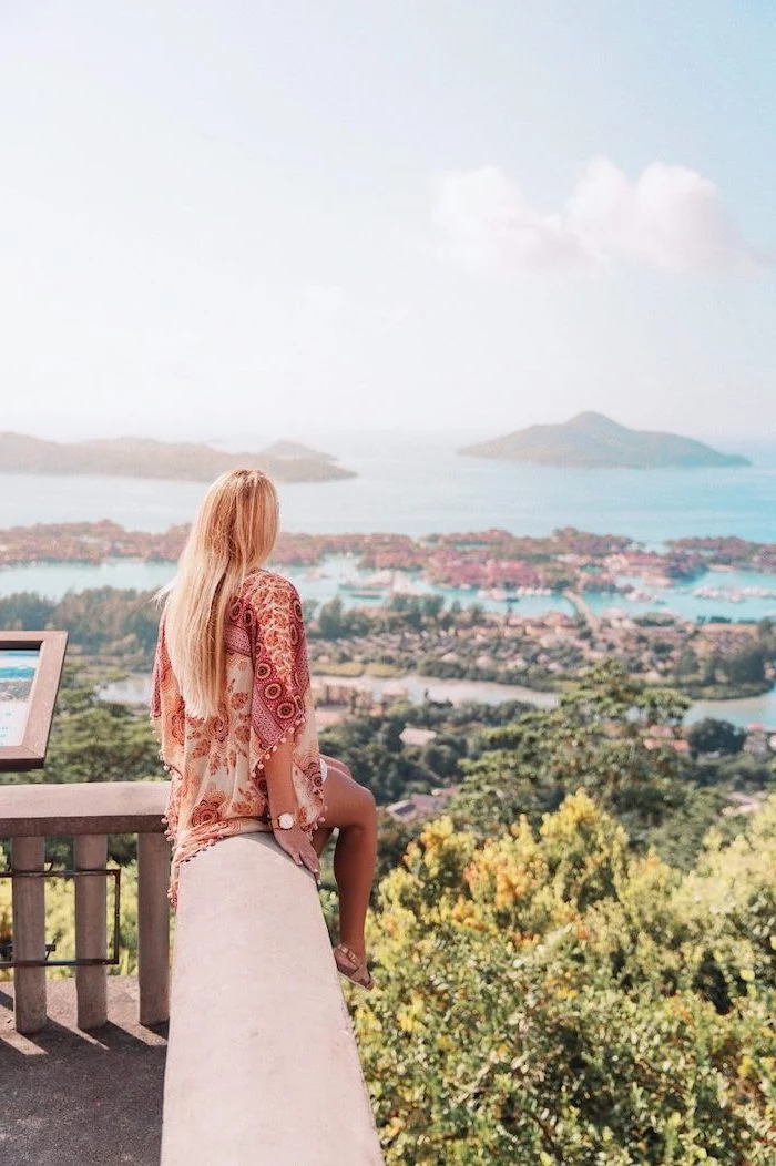 woman sitting on a balcony, with a blonde hair, overlooking the island, seychelles islands