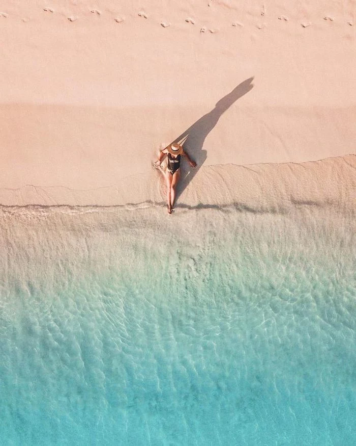 woman sitting on the beach, beach sand, blue water, black swimsuit, digital nomad, seychelles islands